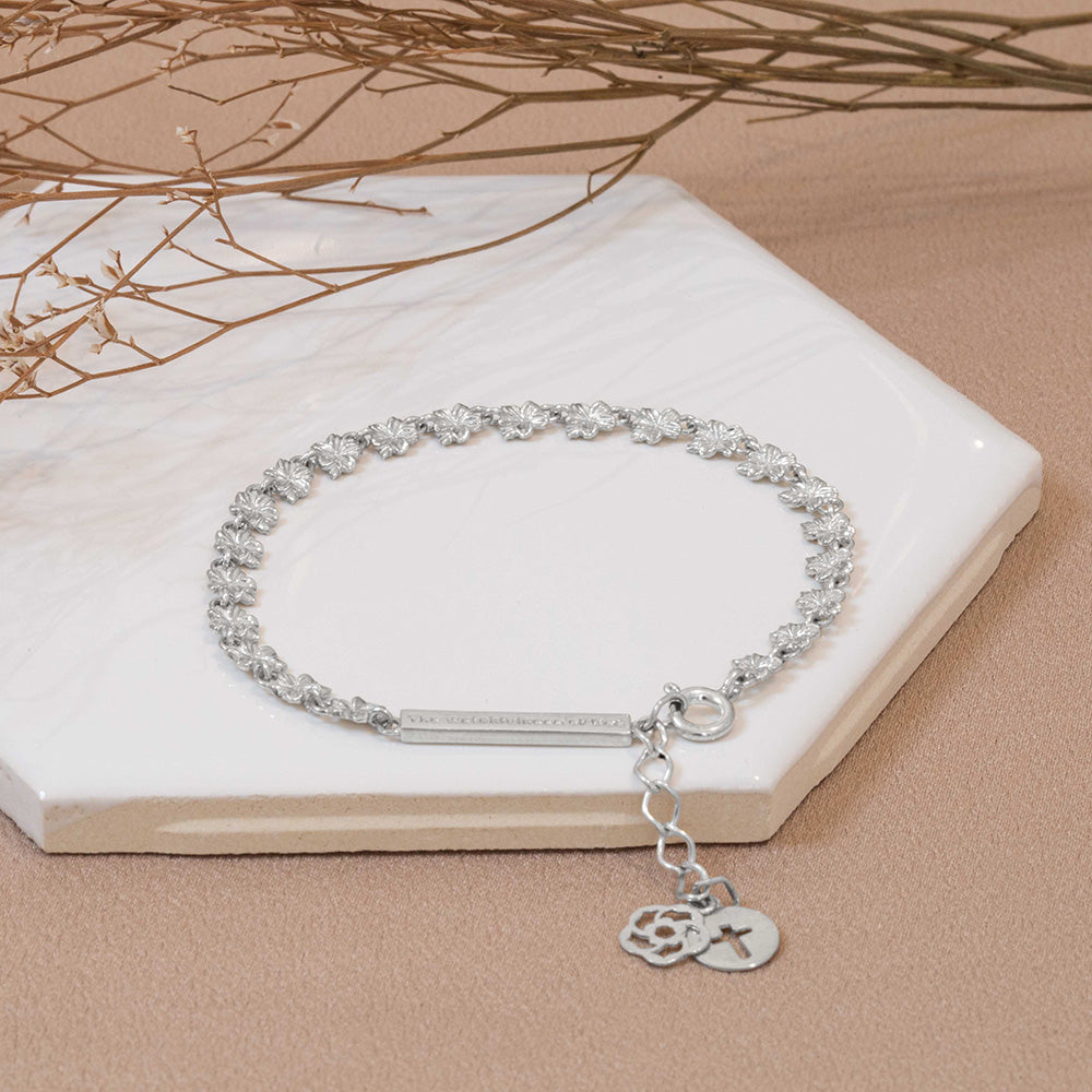 Our Hannah 22 almond blossoms Christian bracelet in sterling silver with our watchfulness of God bar, extension, logo, and the cross displayed on a white tile with dried flower stems  on a light brown fabric background