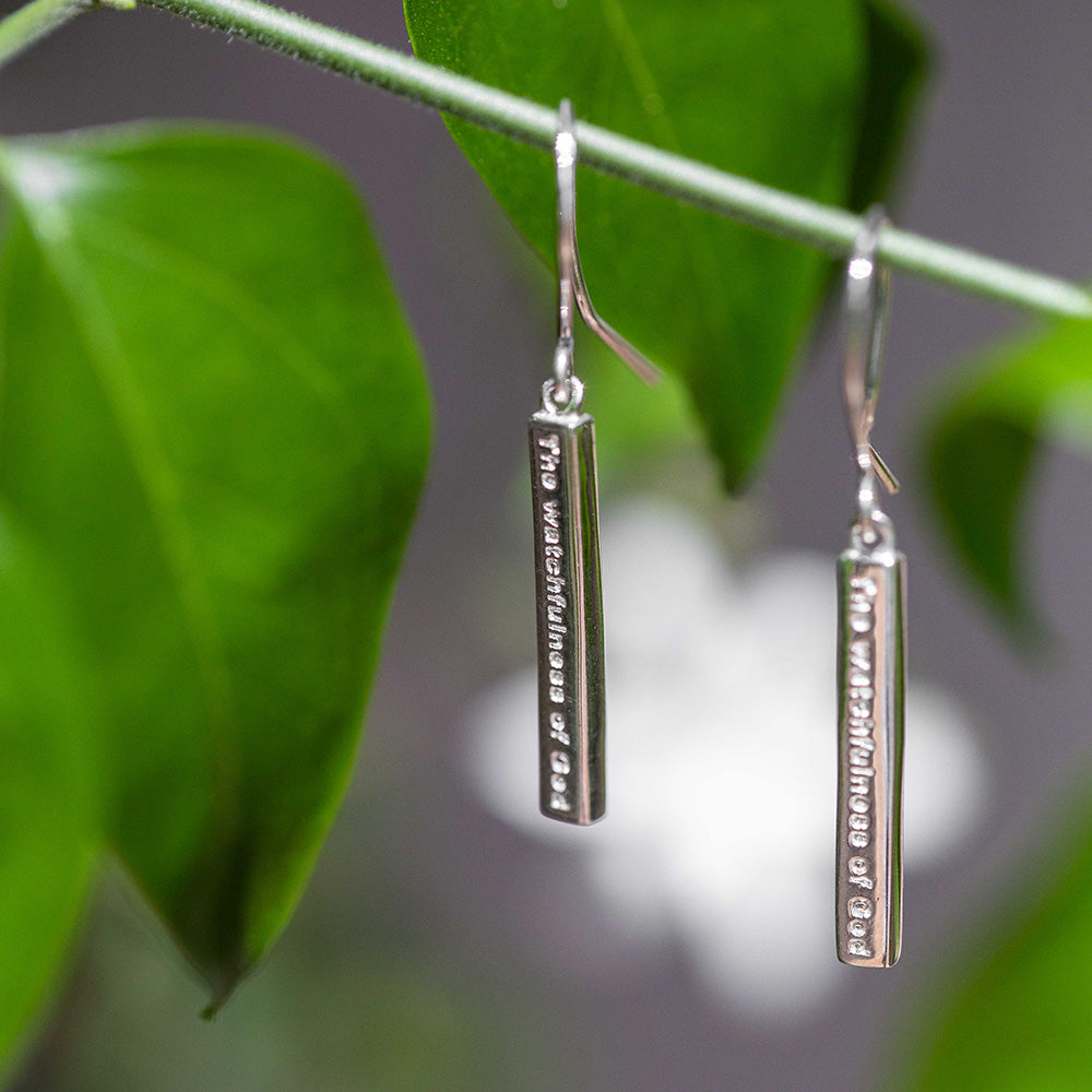 The Watchfulness of God engraved on a sterling silver Bar hook style earrings  serves as a reminder of God's watchful and caring presence in your life. Christian earrings pictured on a stem of green leaves