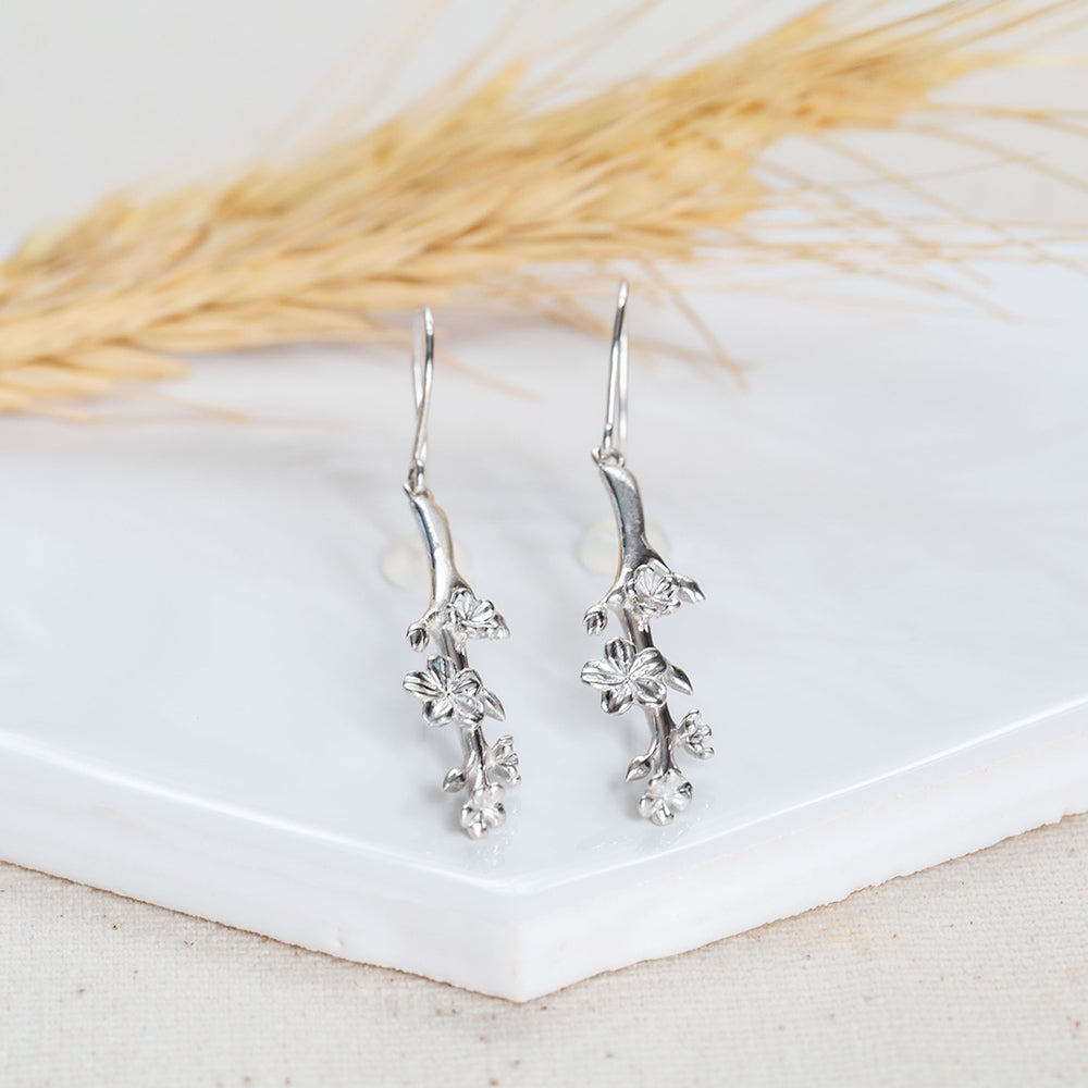 Our Esther Christian Earrings, the branch of an almond tree in sterling silver hook style on a white tile with a wheat husk in the backgound