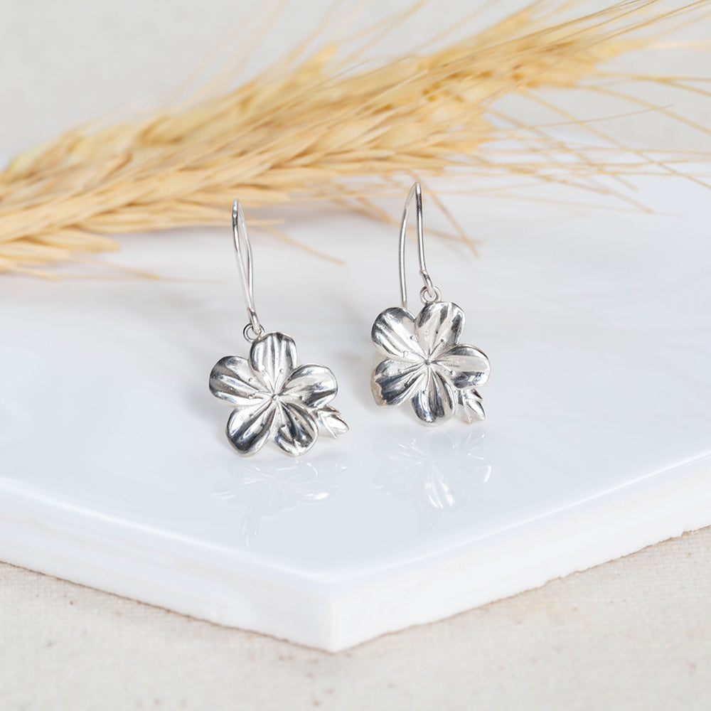 Sterling silver Christian earrings of an almond blossom and bud, inspired by the Word of God as a reminder of His watchfulness over you life. Hook style on a white tile with wheat in the background, from our Mary Magdalene Collection