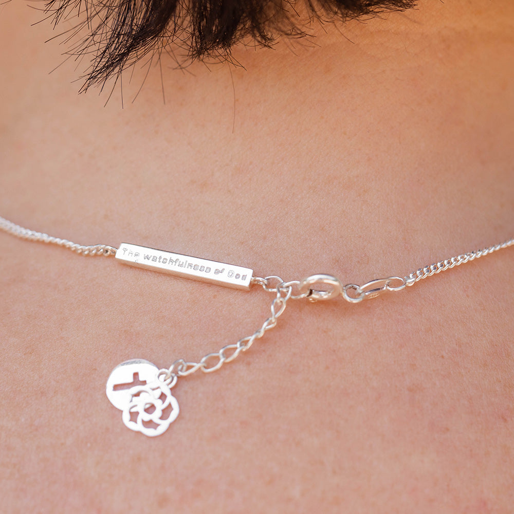  Our watchfulness of God bar, extension with  the cross of Jesus and our logo of an almond blossom dangling off the back of the neck of a short dark haired woman wearing a pink shirt