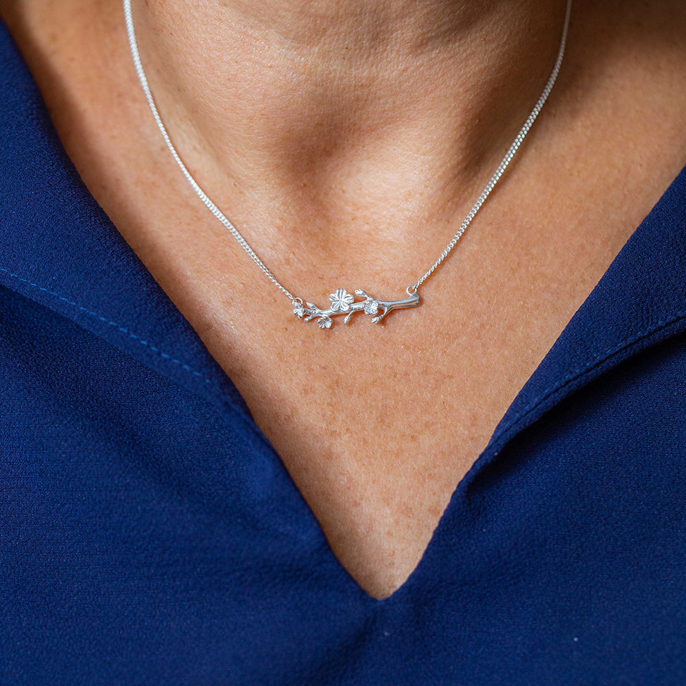  Our Esther Christian necklace, inspired by the branch of an almond tree,  in sterling silver on the neck of a woman wearing a navy blue blouse
