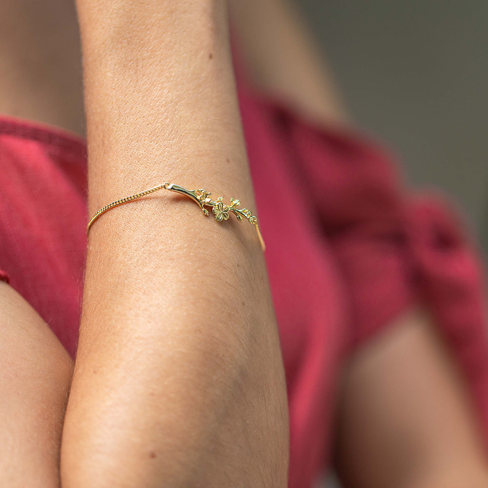 Young woman wearing our christian bracelet Esther, The Branch of an Almond Tree, in yellow gold with a single branch of an Almond Tree with its buds and blossoms. She is wearing a red blouse.