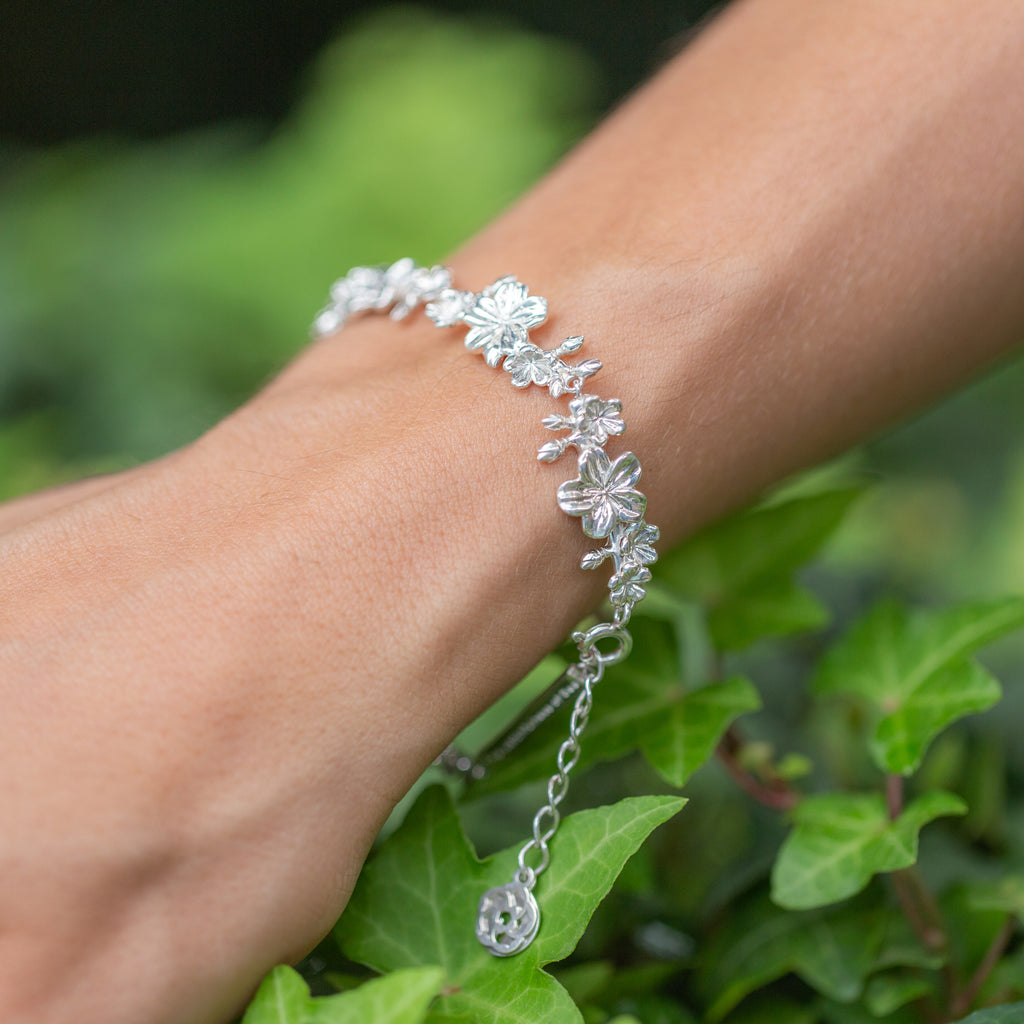 An extended arm of a woman reaching out to green leaves wearing our Esther 22 large almond blossom Christian bracelet in sterling silver.