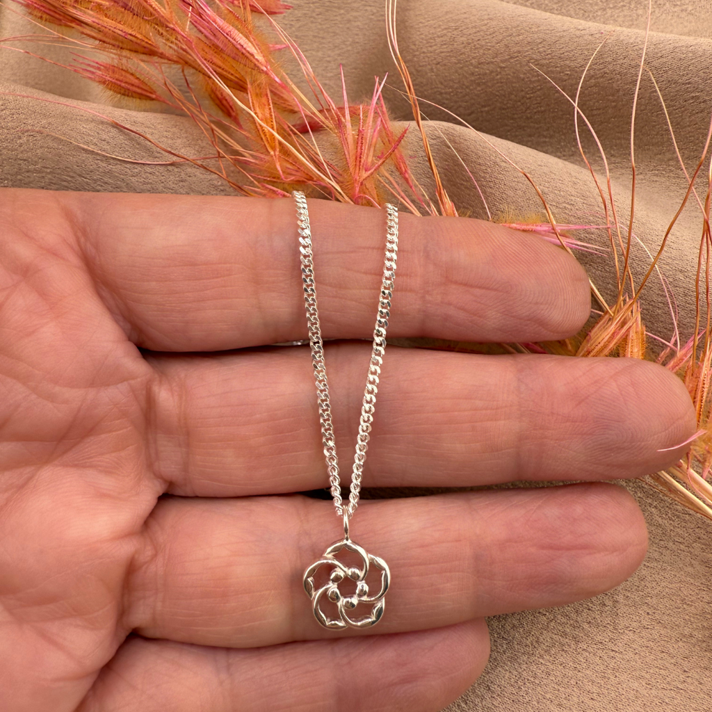 Silver Christian necklace with an almond blossom pendant held in a hand against a beige fabric background