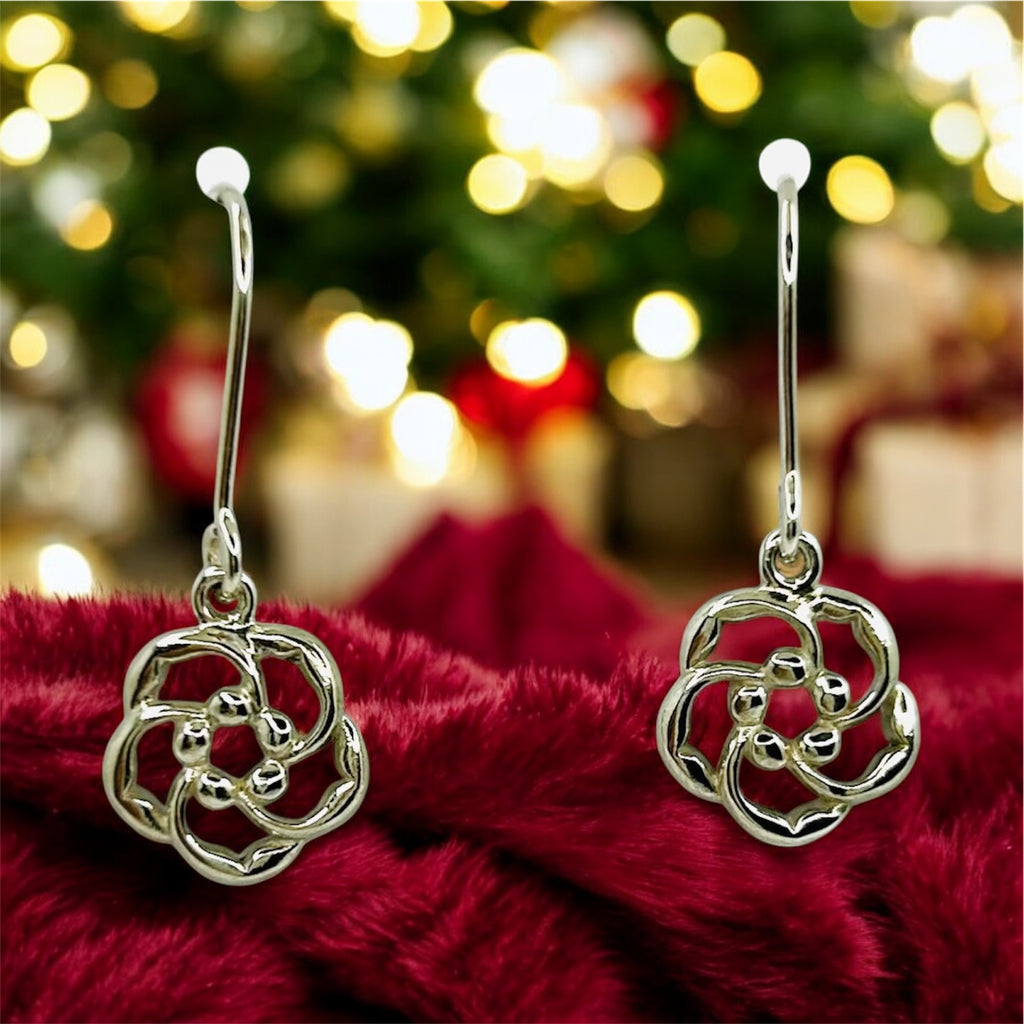 Silver floral earrings on a red fabric background with a blurred Christmas tree and presents in the background.