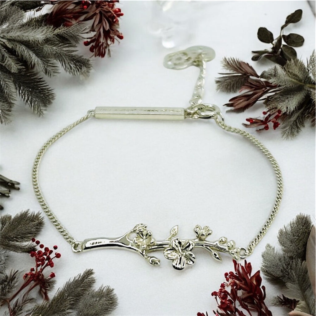 Silver bracelet with floral design on a white background with dried plants