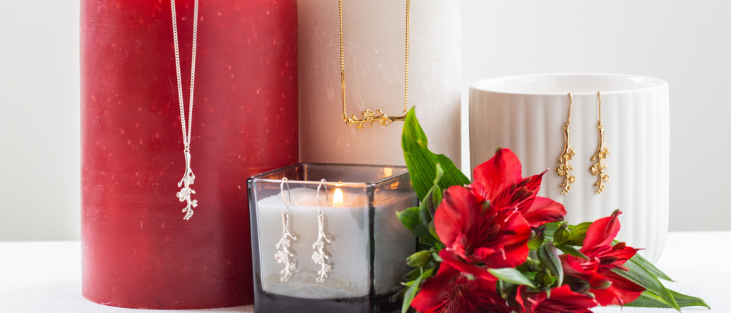 Jewelry including necklaces and earrings displayed with a red candle and potted plant.