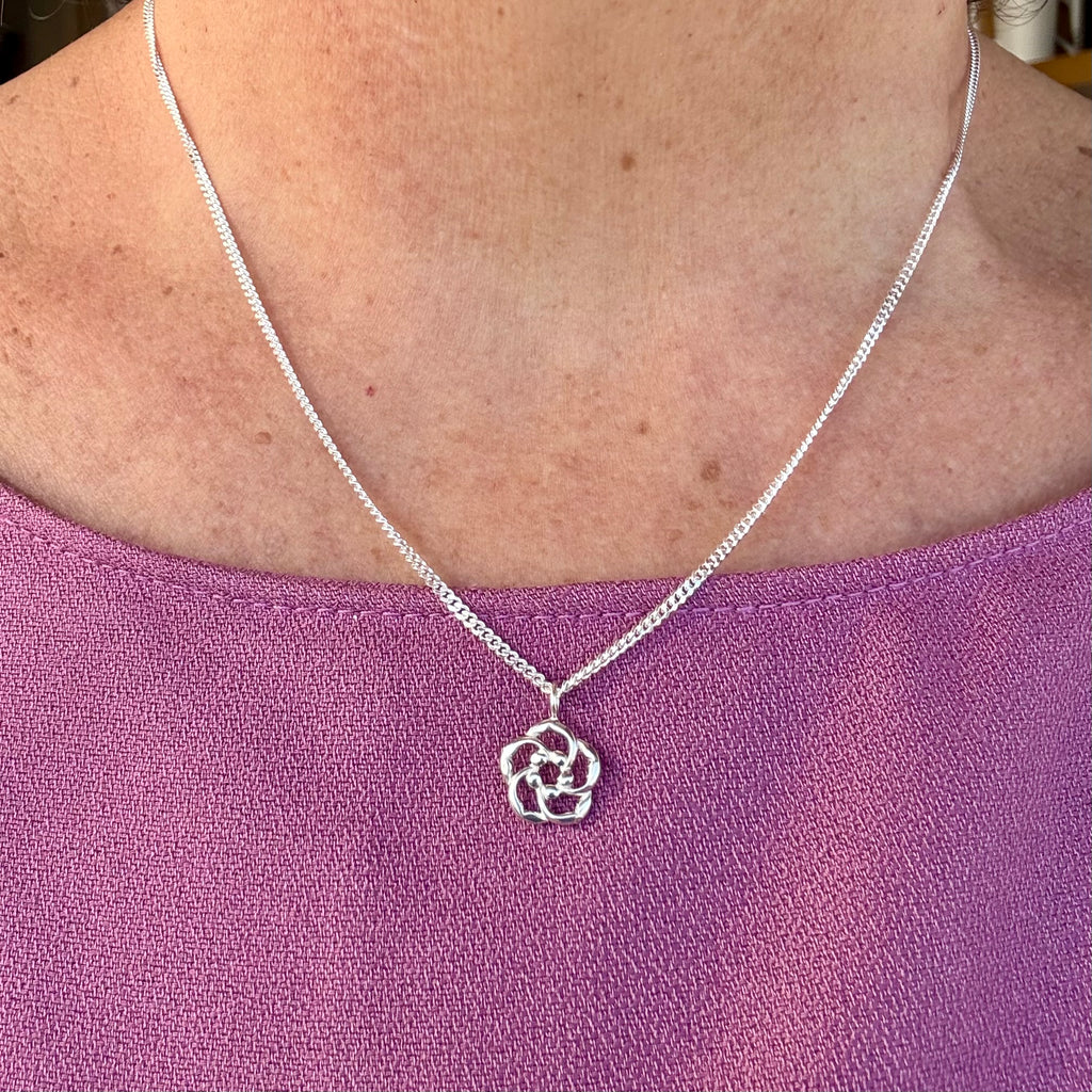 Silver Christian necklace with an almond blossom pendant worn by a person on a purple top
