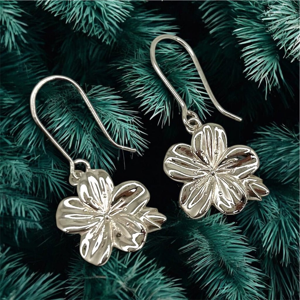 Silver flower-shaped earrings on a green leafy background