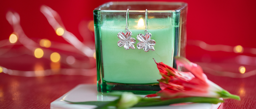 Green candle with silver earrings on top, against a red background with blurred lights