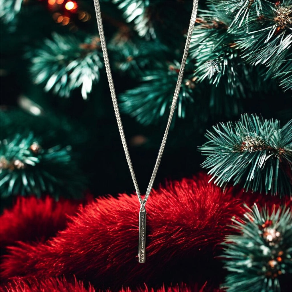 Silver necklace with a pendant on a red fabric background with Christmas tree branches.