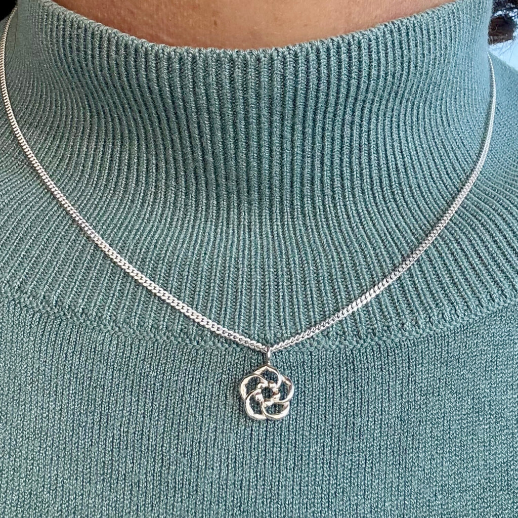 Silver Christian necklace with an almond blossom pendant on a person wearing a teal sweater.