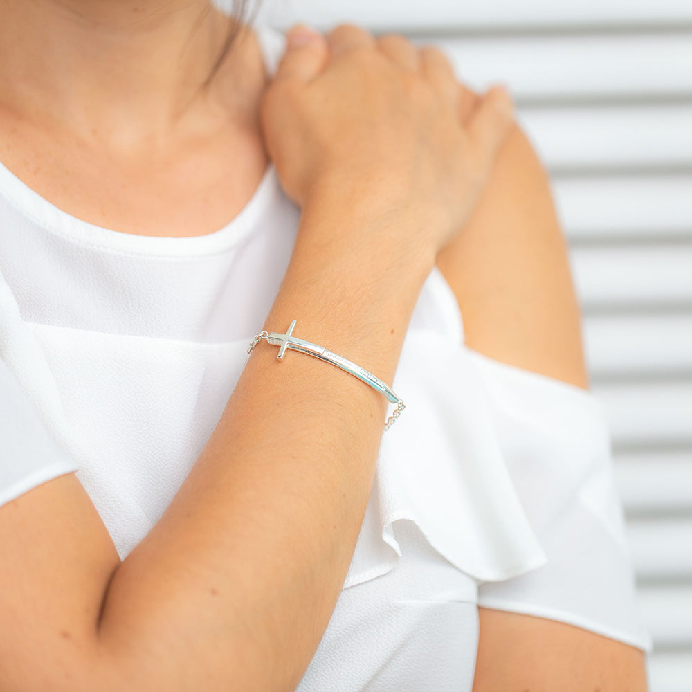Young woman wearing our christian bracelet called Double-Edged Sword in sterling silver in the format of a sword and a cross with "The Watchfulness of God" written on it. She is wearing white blouse and has her hand on her shoulder
