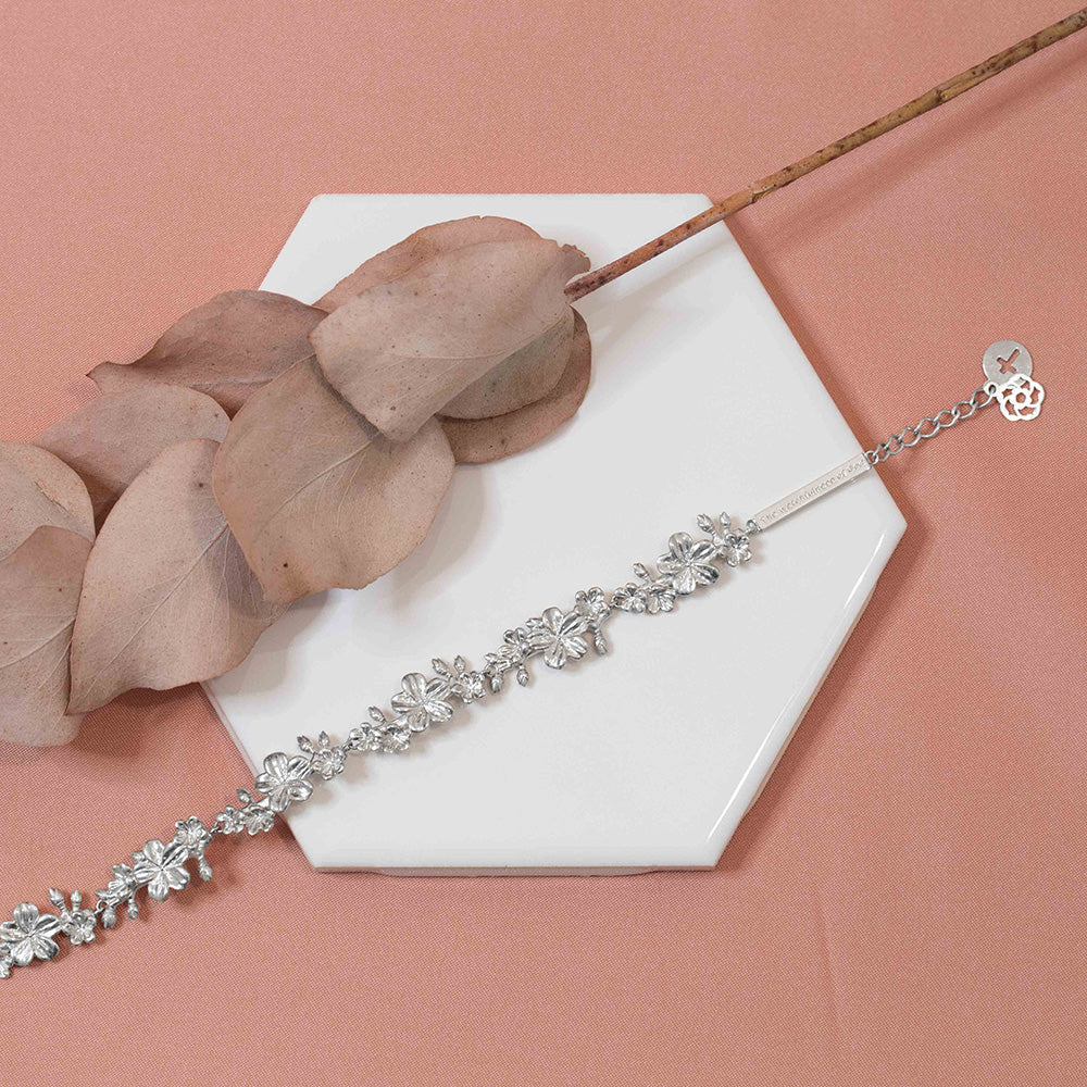 Our Esther 22 large almond blossoms Christian bracelet in sterling silver displayed on a white tile with pink toned leaves and pink fabric background