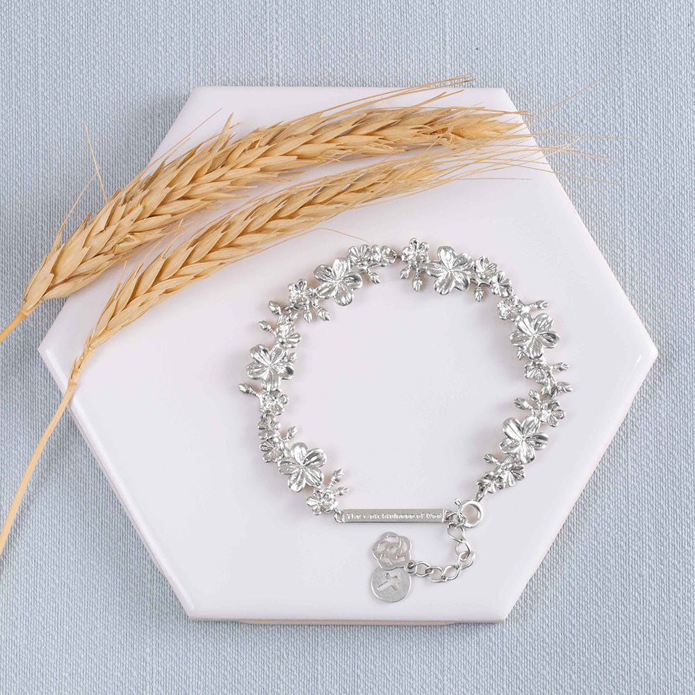 Our Esther 22 large almond blossoms Christian bracelet in sterling silver displayed on a white tile with two stems of wheat