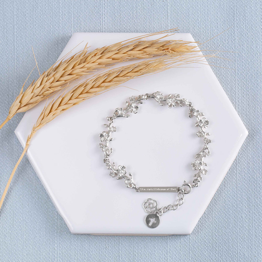 Our Esther 22 small almond blossoms Christian bracelet in sterling silver displayed on a white tile with two stems of wheat on a light blue fabric background