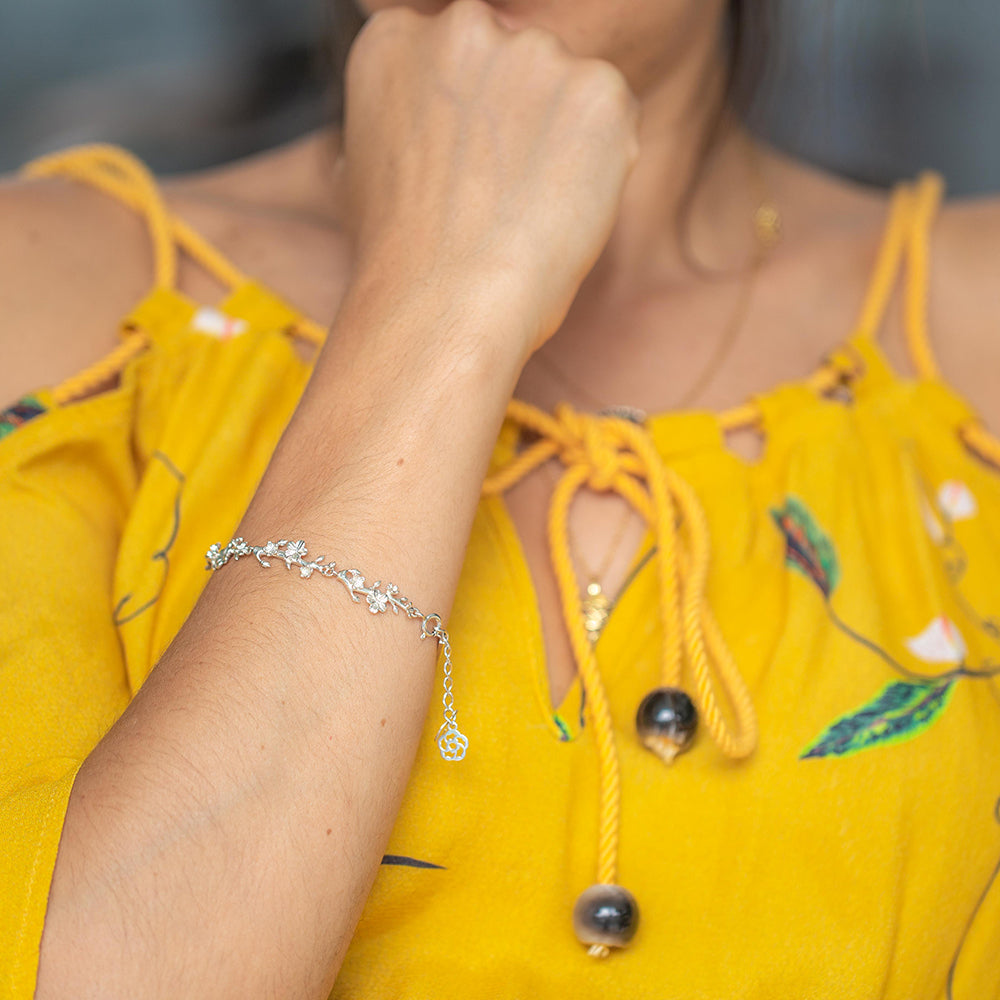 Young woman wearing our christian bracelet Esther 22S in sterling silver with its almond buds and blossom in their branches and the two pendents, one with the cross and the other with our logo. She is wearing a yellow blouse.