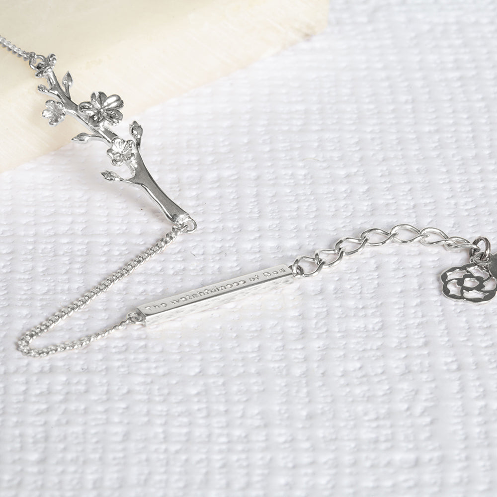 Esther, The Branch of an Almond Tree, christian bracelet in sterling silver with a single branch of an Almond Tree with its buds and blossoms, a bar with "The Watchfulness of God" written on it and two pendents, one with the cross and the other with our logo. The bracelet is on a piece of marble and a write textured paper.