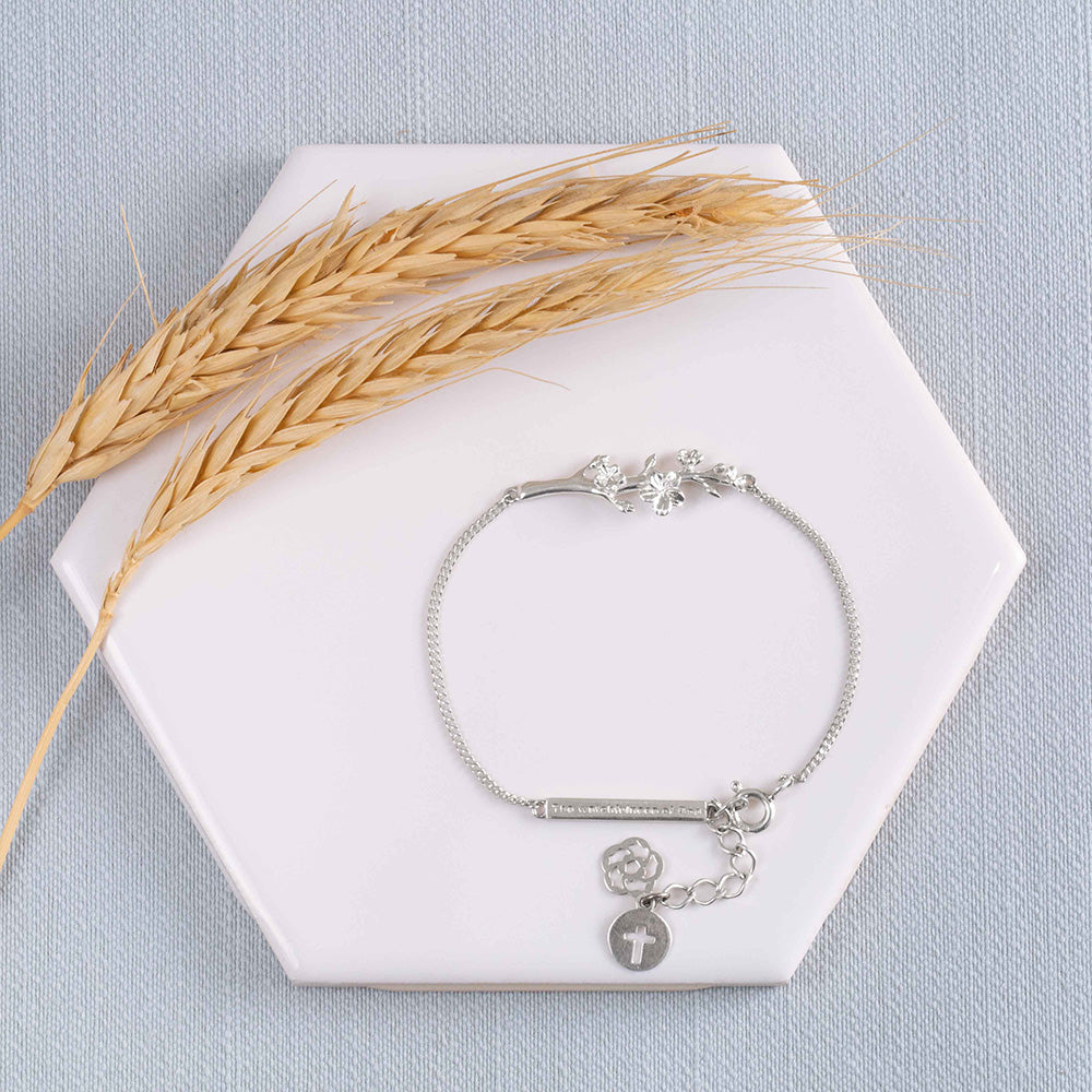 Our Esther  branch of an almond tree Christian bracelet in sterling silver displayed on a white tile with two stems of wheat on a light blue fabric background.