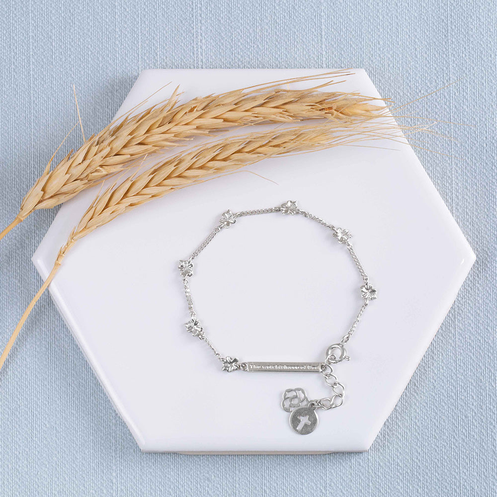 Our Hannah 7 almond blossoms Christian bracelet in sterling silver displayed on a white tile with two stems of wheat on a light blue textured fabri background.