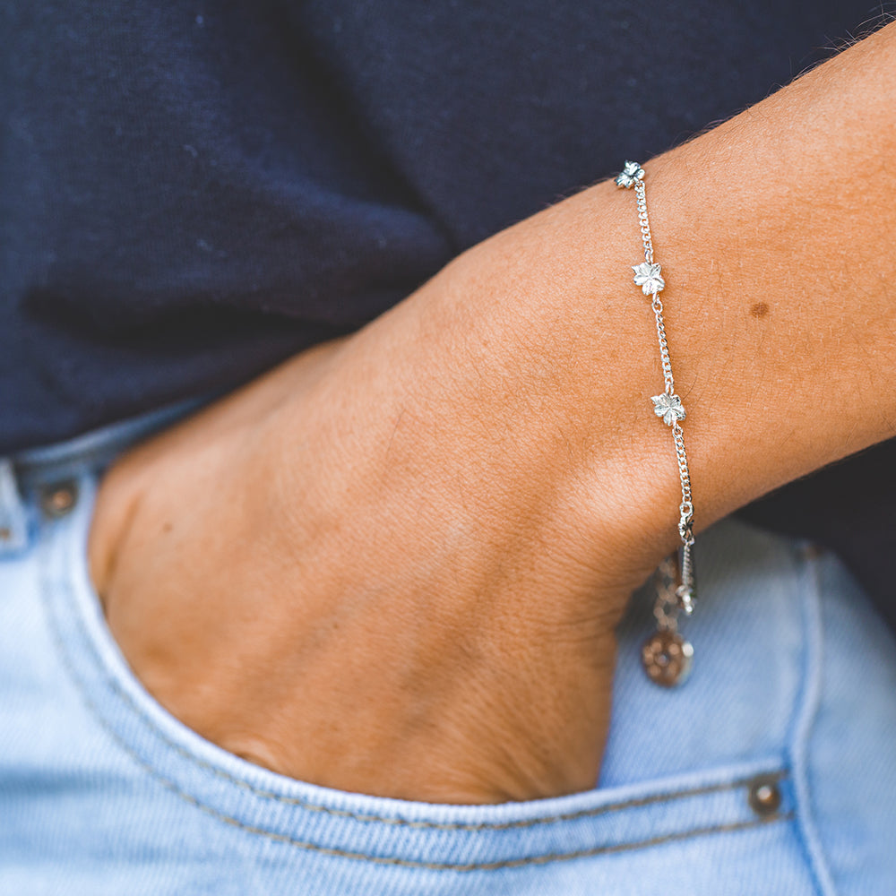 Young woman wearing our christian bracelet Hannah 7, in sterling silver, inspired by the lampstand of the tabernacle with 7 almond blossoms and buds, 7 being the biblical number of completion and perfection with the pendants dangling on the side. She has her hand in the pocket of her blue jeans and she is wearing a blue blouse.