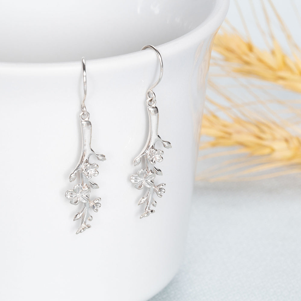 Our Esther Christian Earrings, the branch of an almond tree in sterling silver hook style dangling off of a white coffee cup 