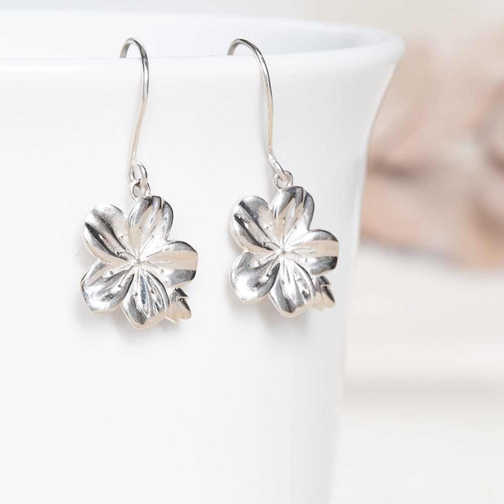 Sterling silver Christian earrings of an almond blossom and bud, inspired by the Word of God as a reminder of His watchfulness over you life. Hook style on a white coffee cup from our Mary Magdalene Collection