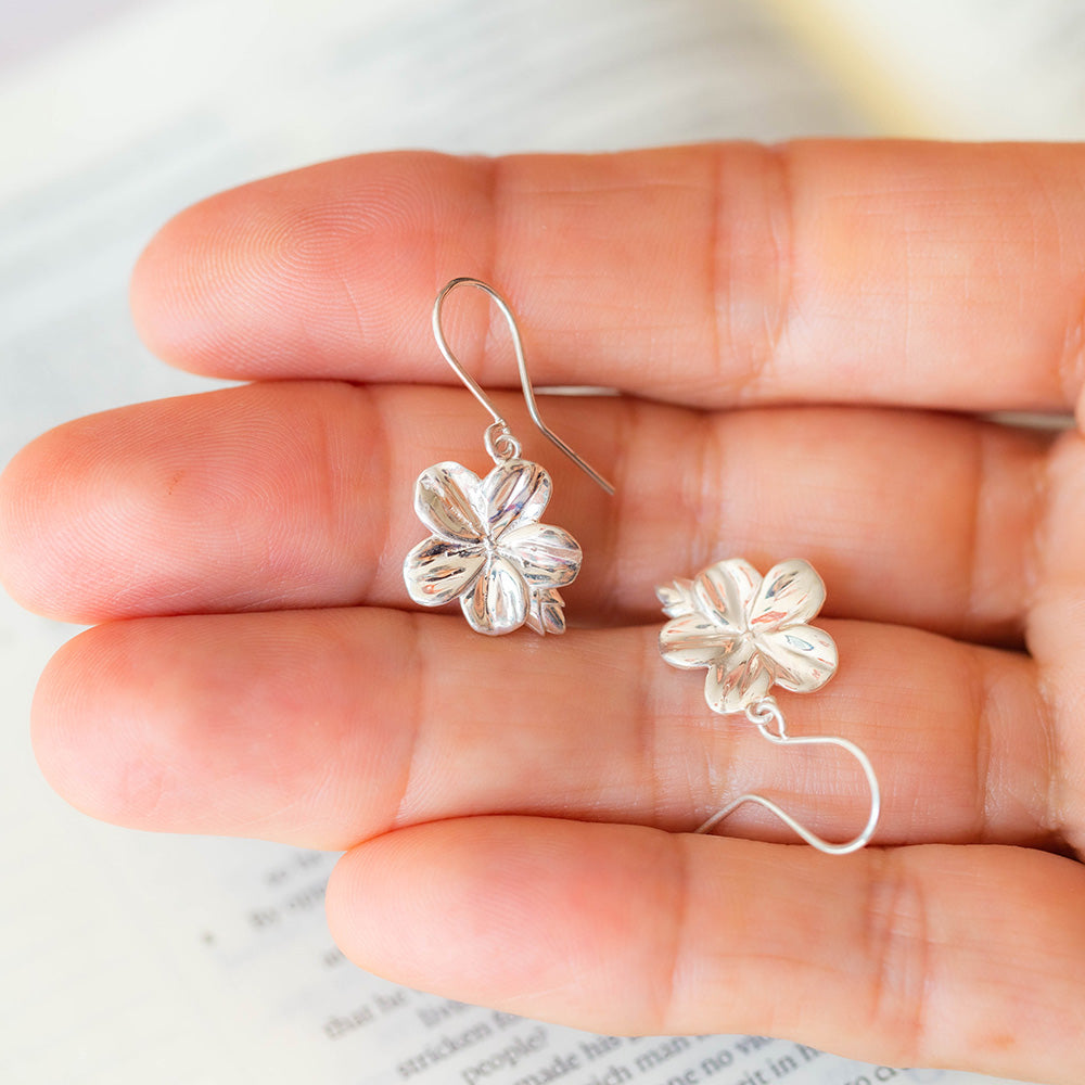 Inspired by the symbolism of the Almond Blossom, these earrings serve as a reminder that God is constantly watching over you. Christian earrings in sterling silver hook style on a womans hand with an open Bible in the background. From our Mary Magdalene Collection