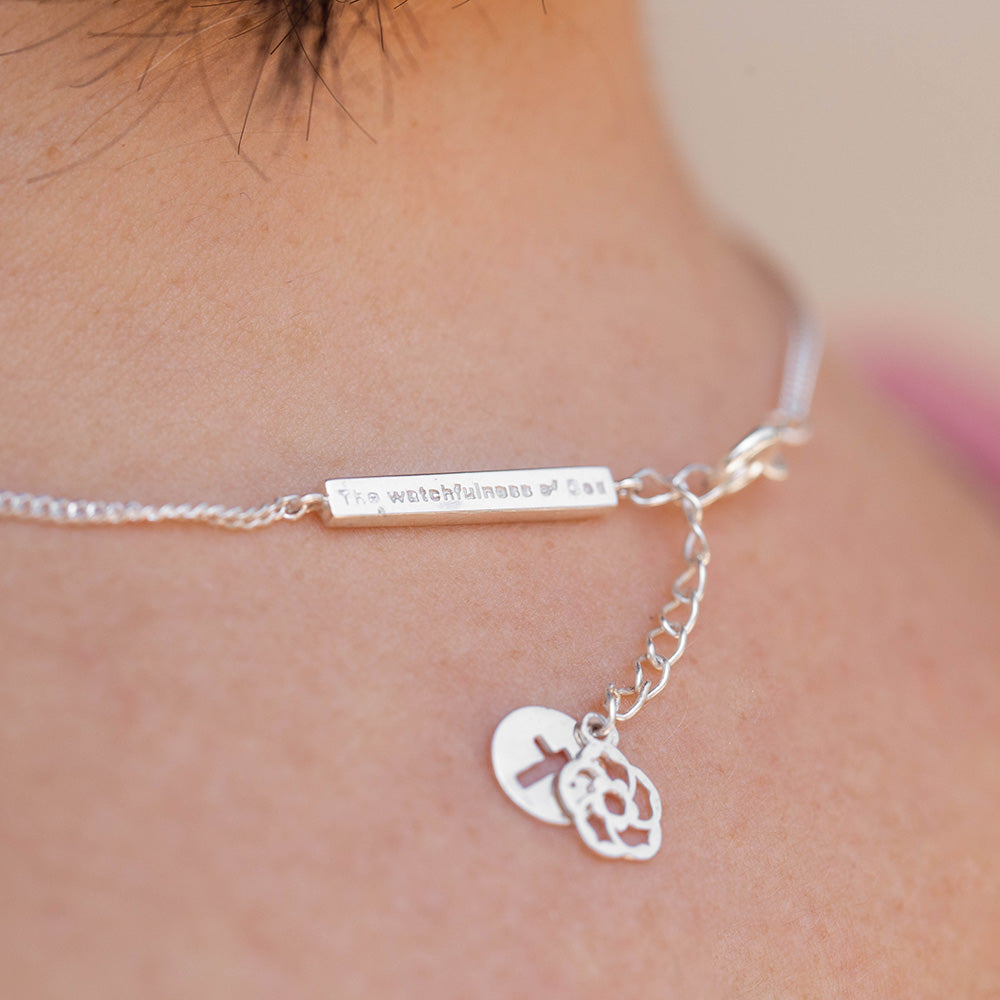 Our watchfulness of God bar, extension with the cross of Jesus and our logo of an almond blossom dangling off the back of the neck of a short dark haired woman wearing a pink shirt