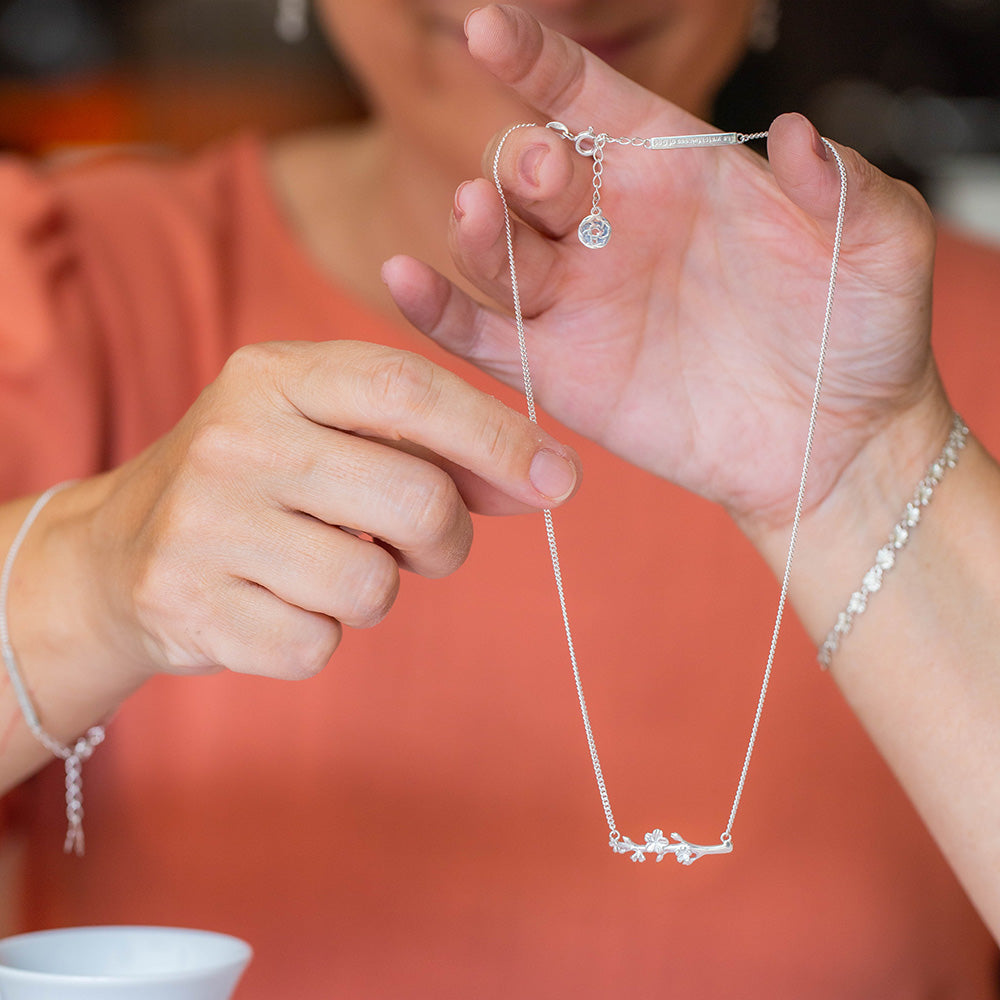  Our Esther Christian necklace inspired by the branch of an almond tree, in sterling silver in the hands of a woman wearing an orange blouse