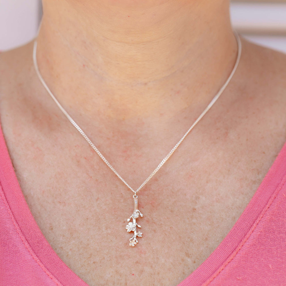Our Esther Christian necklace the branch of an almond tree in sterling silver on the neck of a woman wearing a pink blouse.