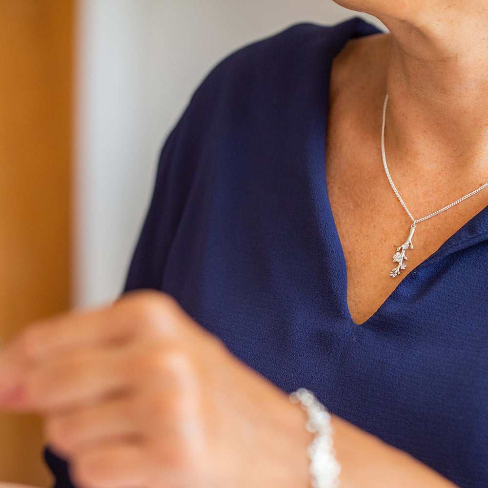 Our Esther Christian necklace the branch of an almond tree in sterling silver on the neck of a woman wearing a navy blue blouse.