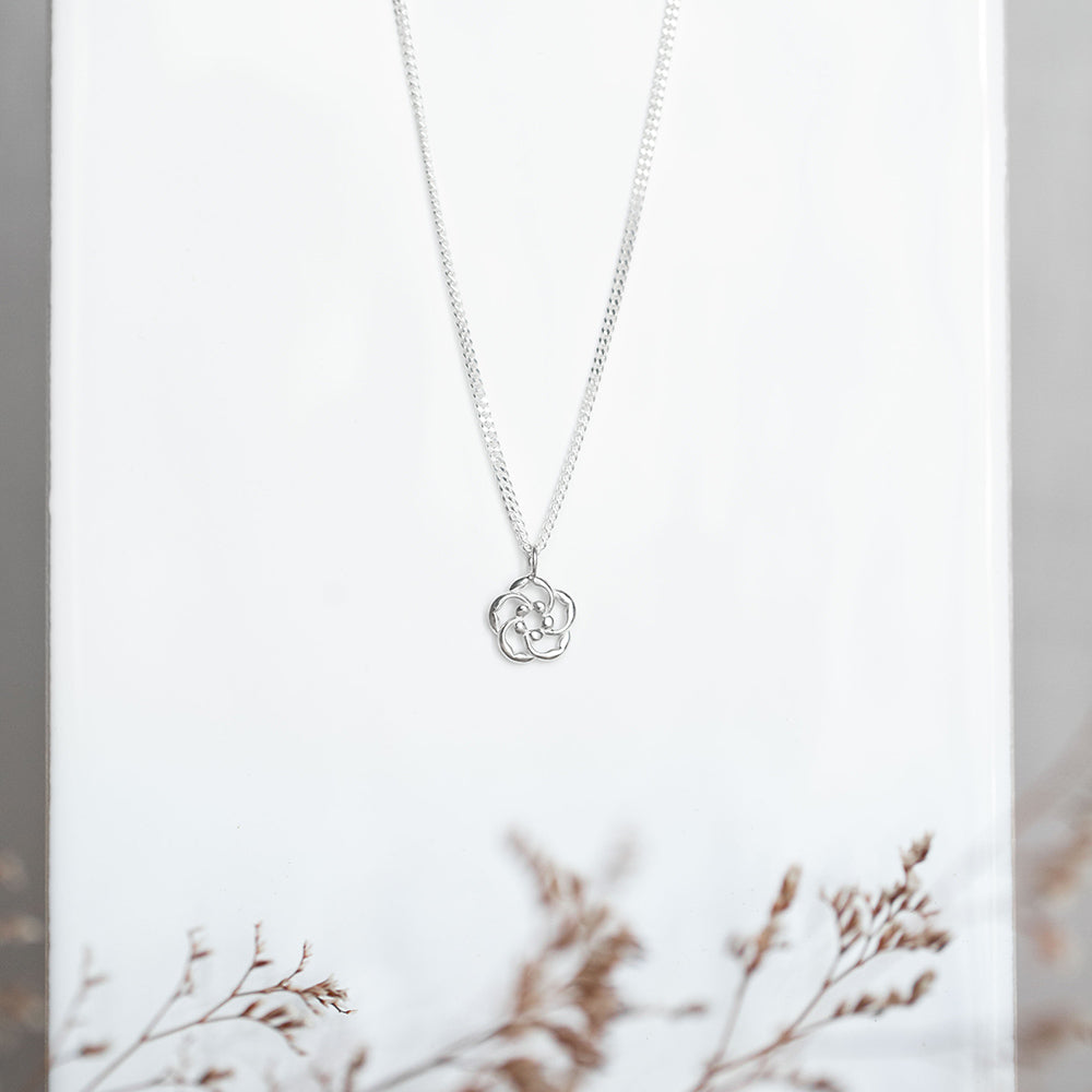 Our almond blossom logo Christian necklace in sterling silver as a reminder that God is lovingly watching over you at all times.. Pictured in a white background with dried flowers