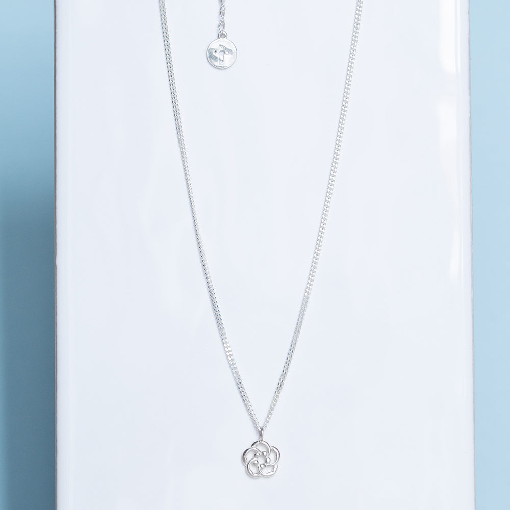 Our almond blossom logo Christian necklace in sterling silver as a reminder that God is lovingly watching over you at all times.. Pictured in a white tile on a light blue background