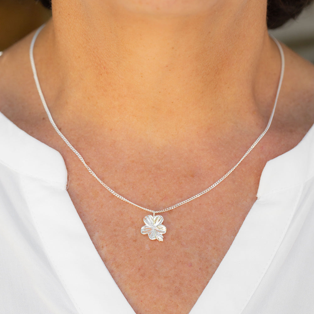 A woman in a white blouse wearing our Mary Magdalene Christian necklace of an almond blossom and bud in sterling silver inspired by the meaning of the almond blossom in the Word of God and serves as a reminder of His watchfulness over your life.