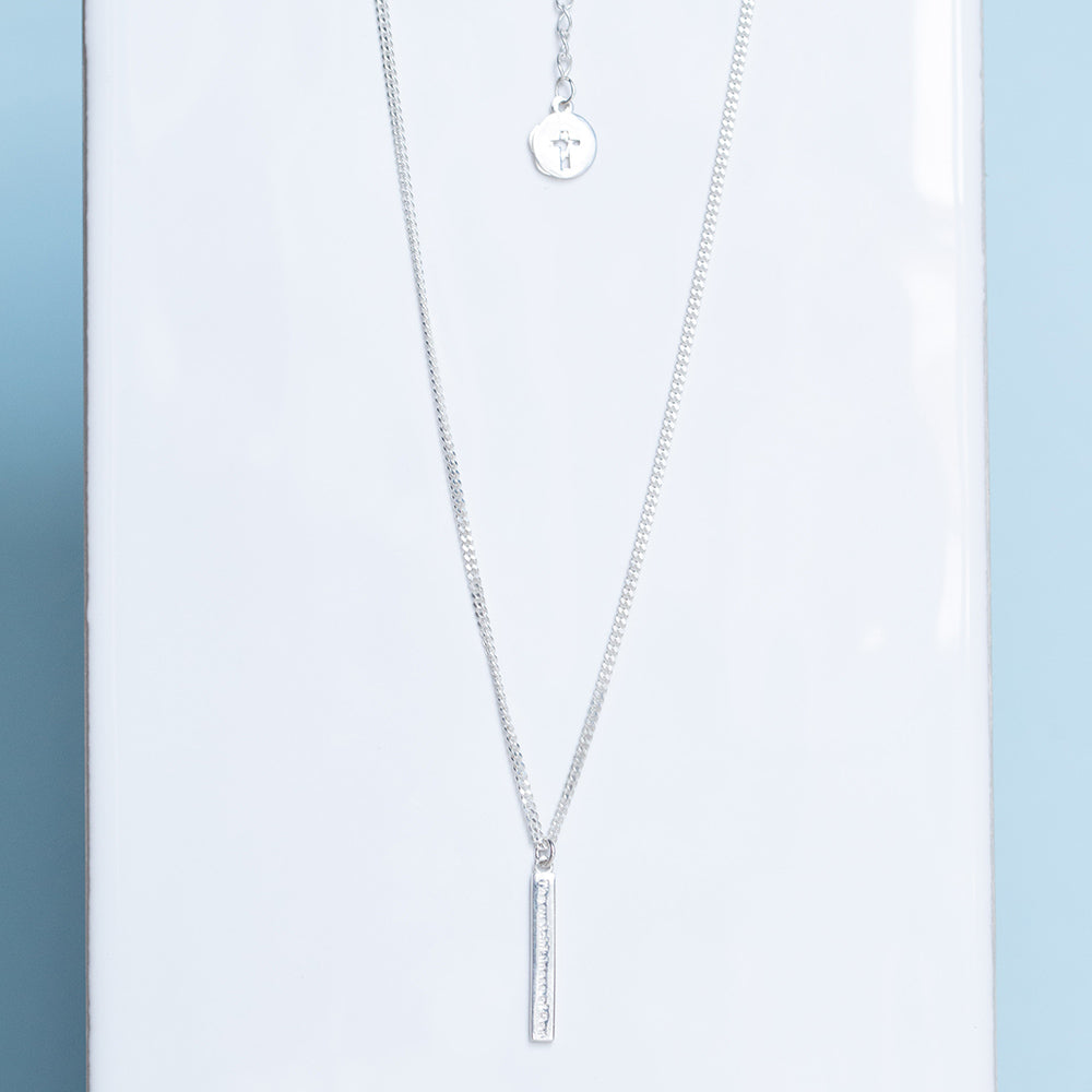 The Watchfulness of God engraved on a sterling silver bar necklace  serves as a reminder of God's watchful and caring presence in your life. Christian necklace with and extension of the cross of Jesus and our logo of an almond blossom on a white tile background