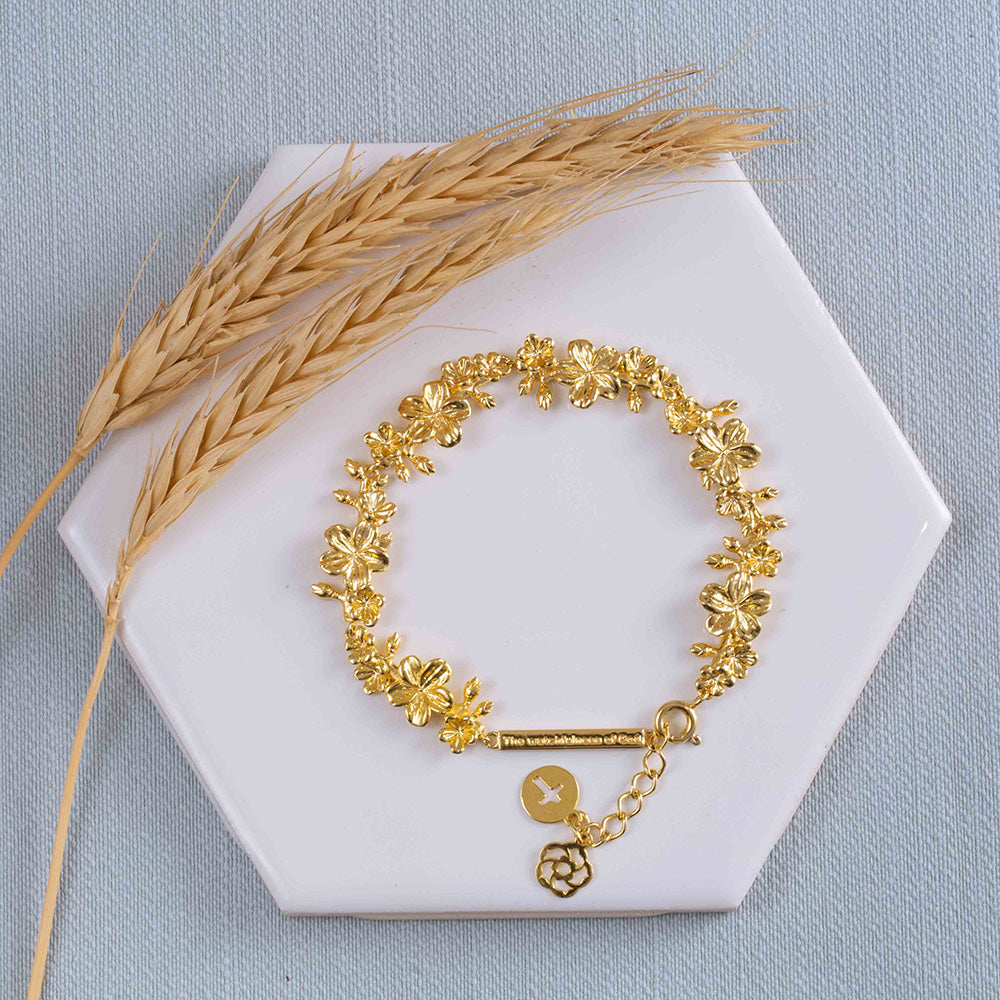 Our Esther 22 large almond blossoms Christian bracelet gold plated over sterling silver displayed on a white tile with two stems of wheat on light blue fabric