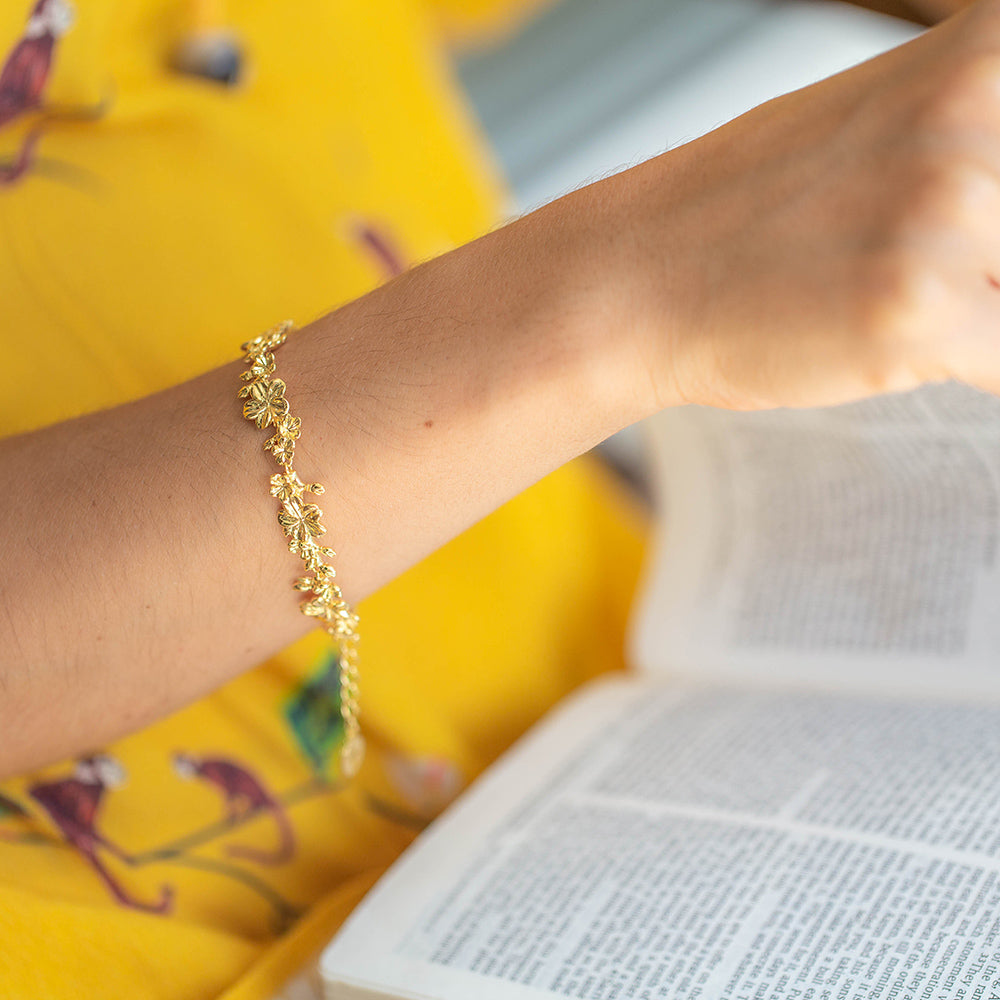 Young woman wearing our christian bracelet Esther 22L in yellow gold with its almond buds and blossom in their branches. She is wearing a yellow blouse and is reading the Bible.