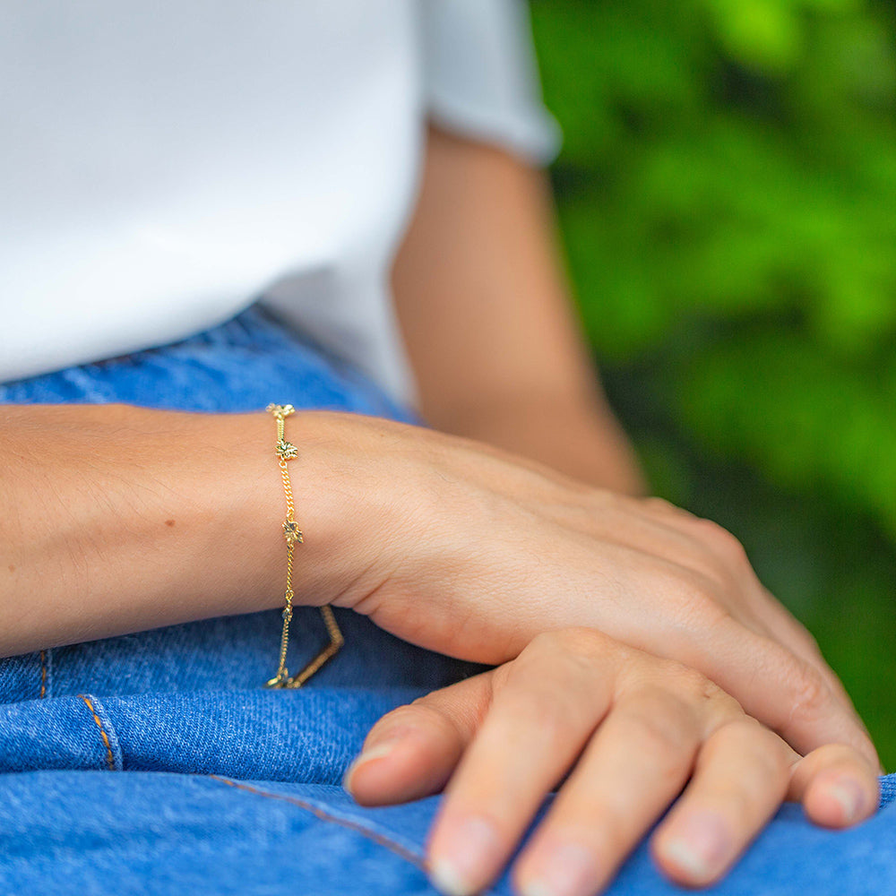 Young woman wearing our christian bracelet Hannah 7, in yellow gold, inspired by the lampstand of the tabernacle with 7 almond blossoms and buds, 7 being the biblical number of completion and perfection with the pendants dangling on the side. She has her hand in her lap and she is wearing a white blouse and a jeans skirt.