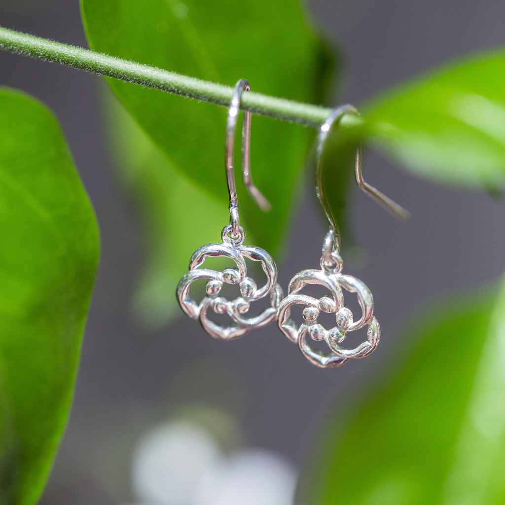 Our almond blossom logo Christian earrings in sterling silver, hook style dangling on a stem of green leaves, serve as a reminder that God is always watching over you.